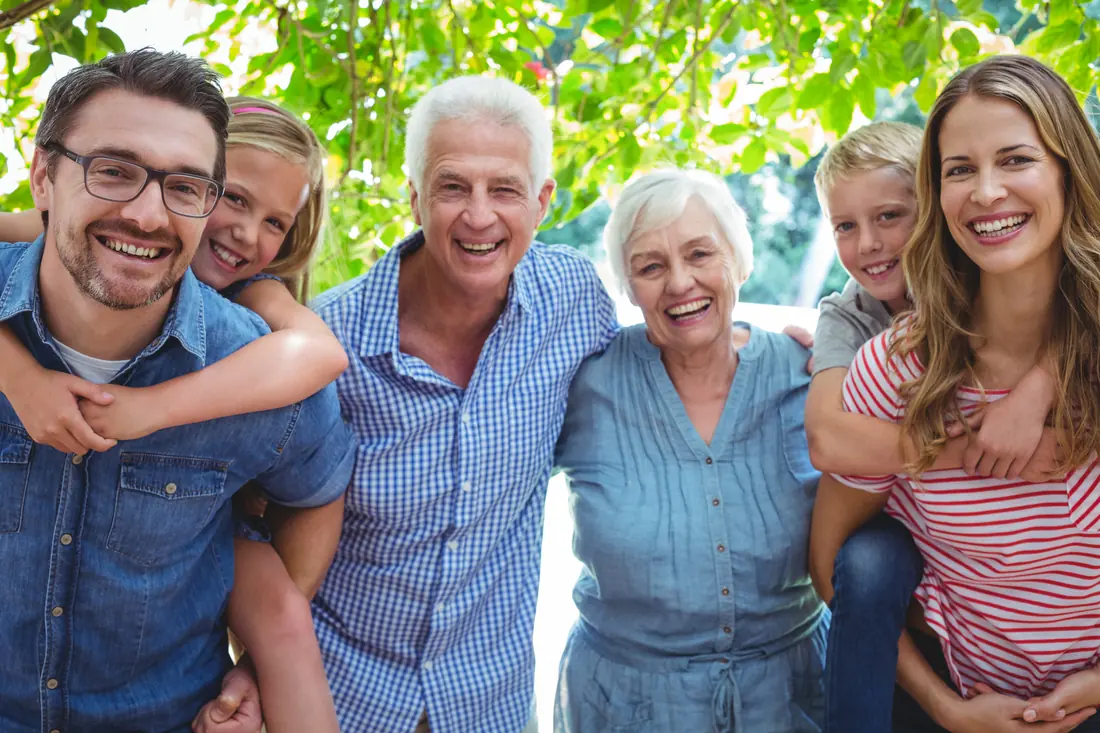 Drei Generationen einer Familie stehen lachend zusammen im Garten