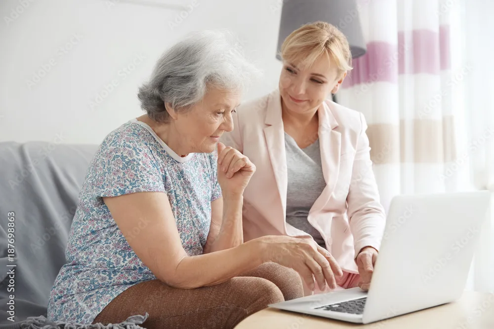 Beraterin schaut gemeinsam mit einer Seniorin auf einen Laptop