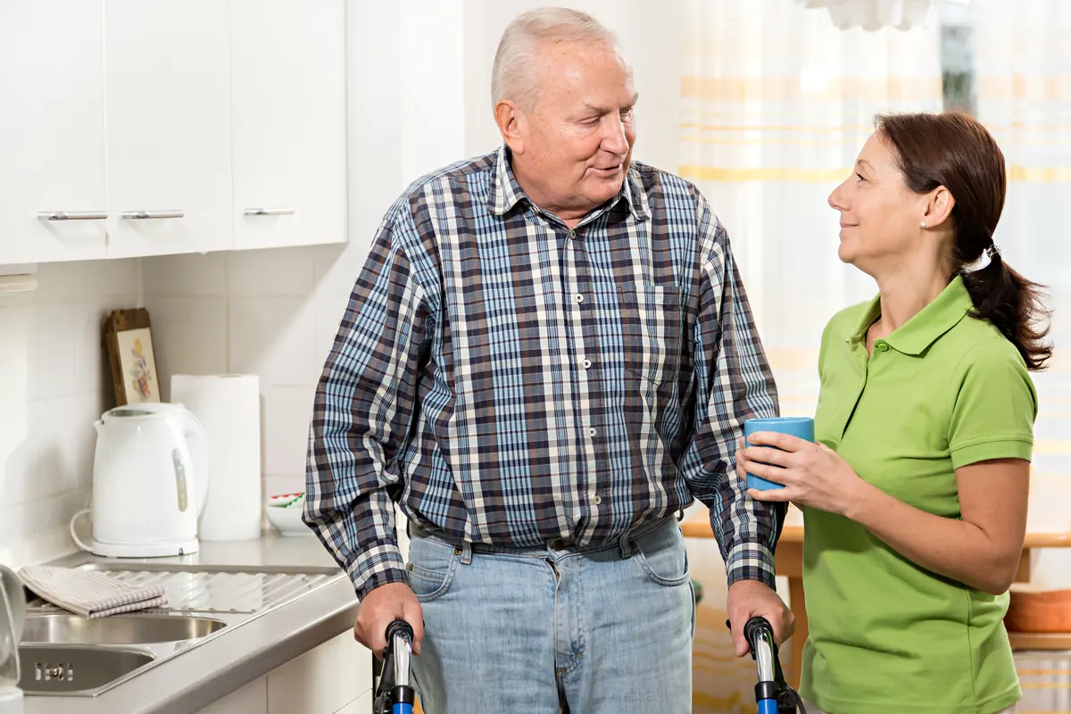 Alltagsbegleiterin unterhält sich mit einem älteren Herrn mit Rollator in der Küche