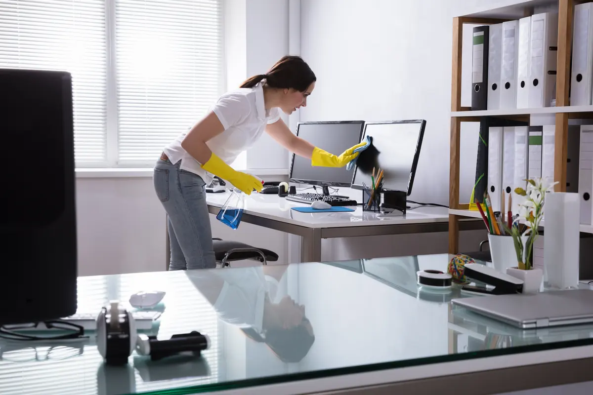 Reinigungskraft wischt einen Schreibtisch in einem hellen Büro ab