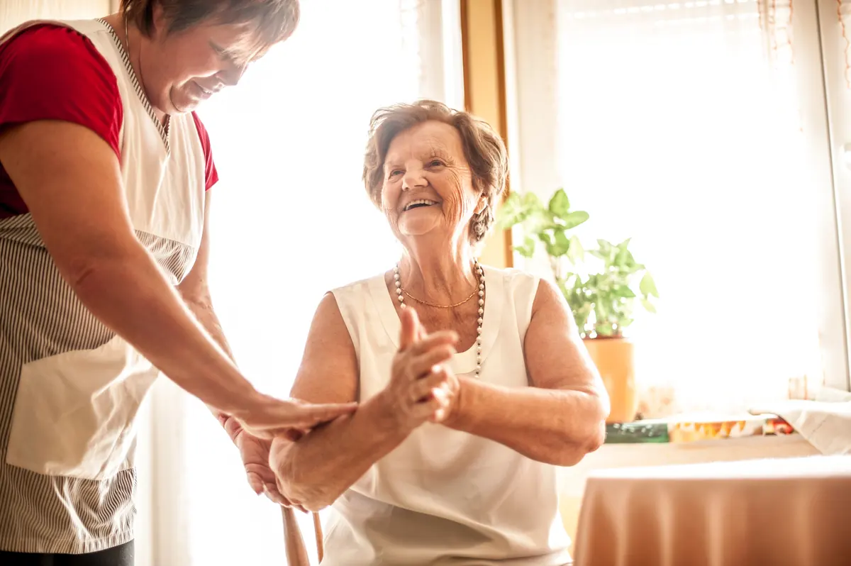 Haushaltshilfe und Seniorin lachen gemeinsam in der Küche
